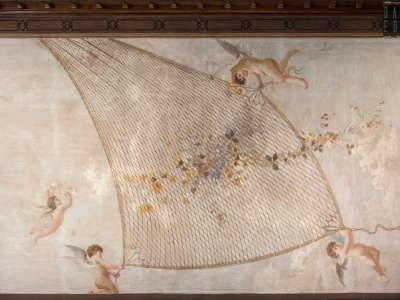 ...sulla quale, su un lucente cielo di sfondo, svolazzano amorini intenti a reggere una rete con ghirlande floreali